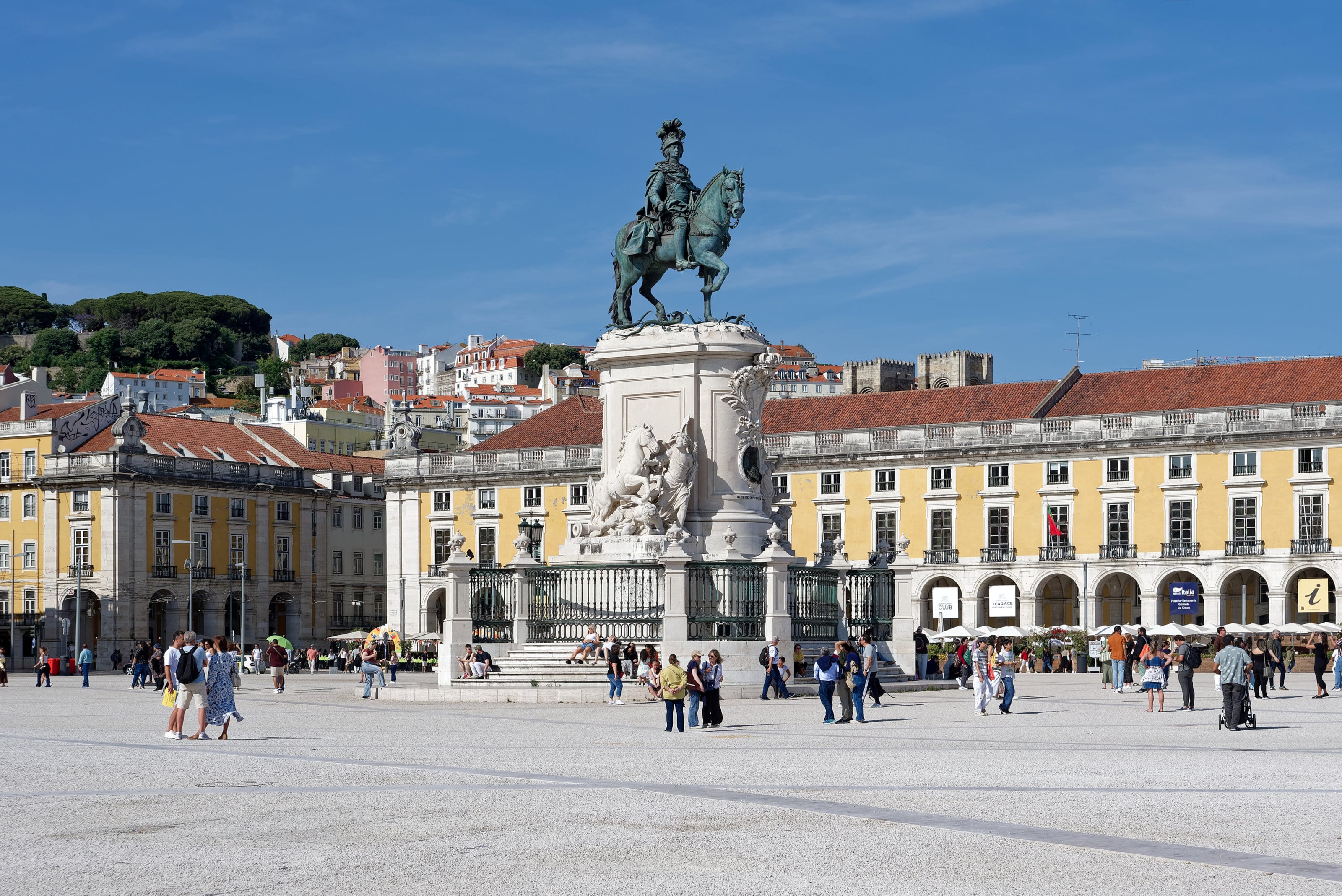 Estátua equestre na Praça do Comércio, cercada por prédios amarelos, em Lisboa.