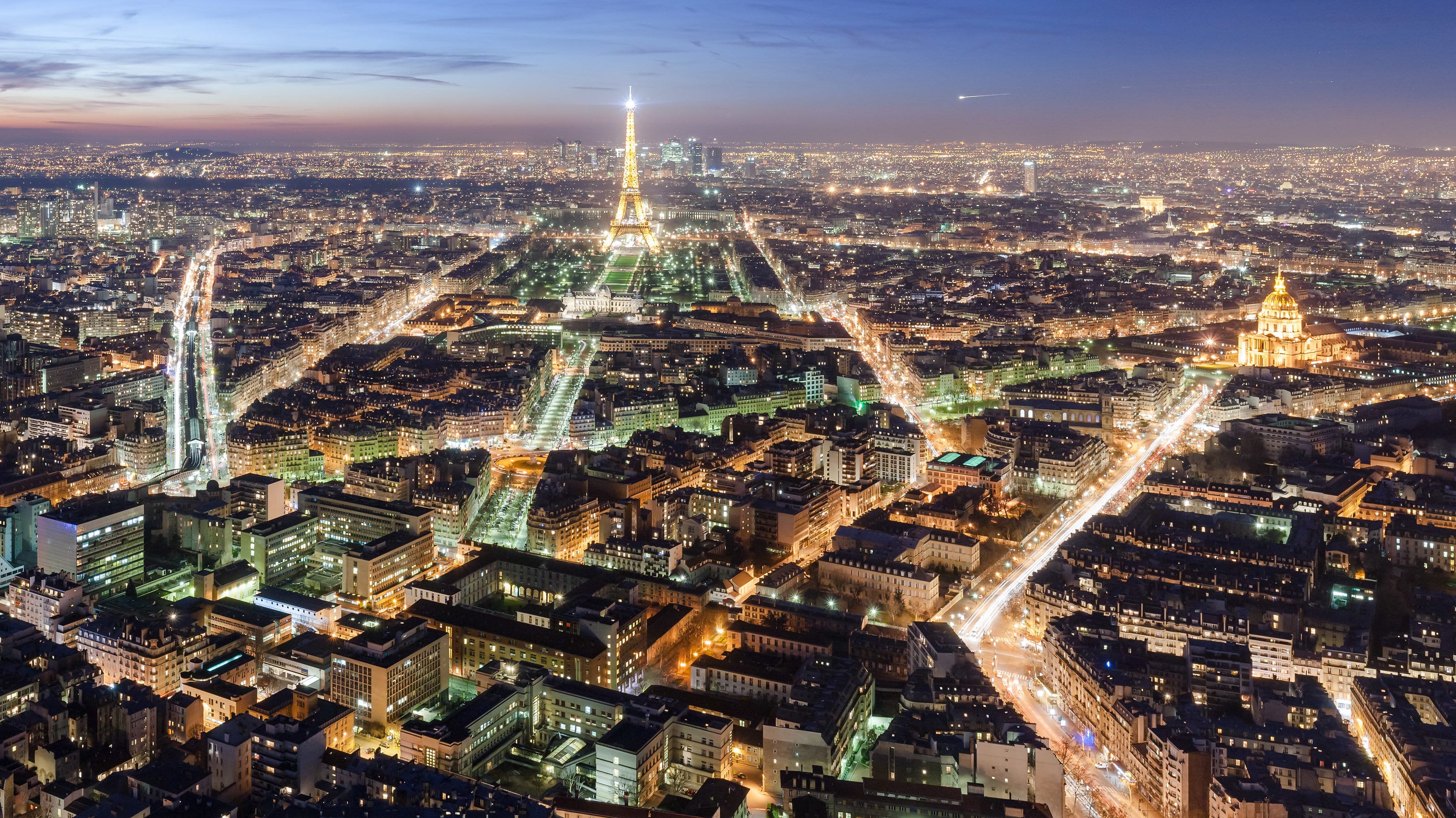 Vista aérea noturna de Paris iluminada, com a Torre Eiffel ao fundo.