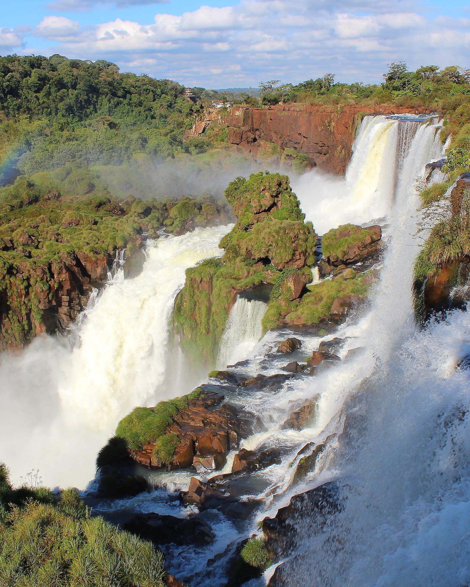 Quedas d'água cercadas de mata, com um arco-íris, nas Cataratas do Iguaçu.