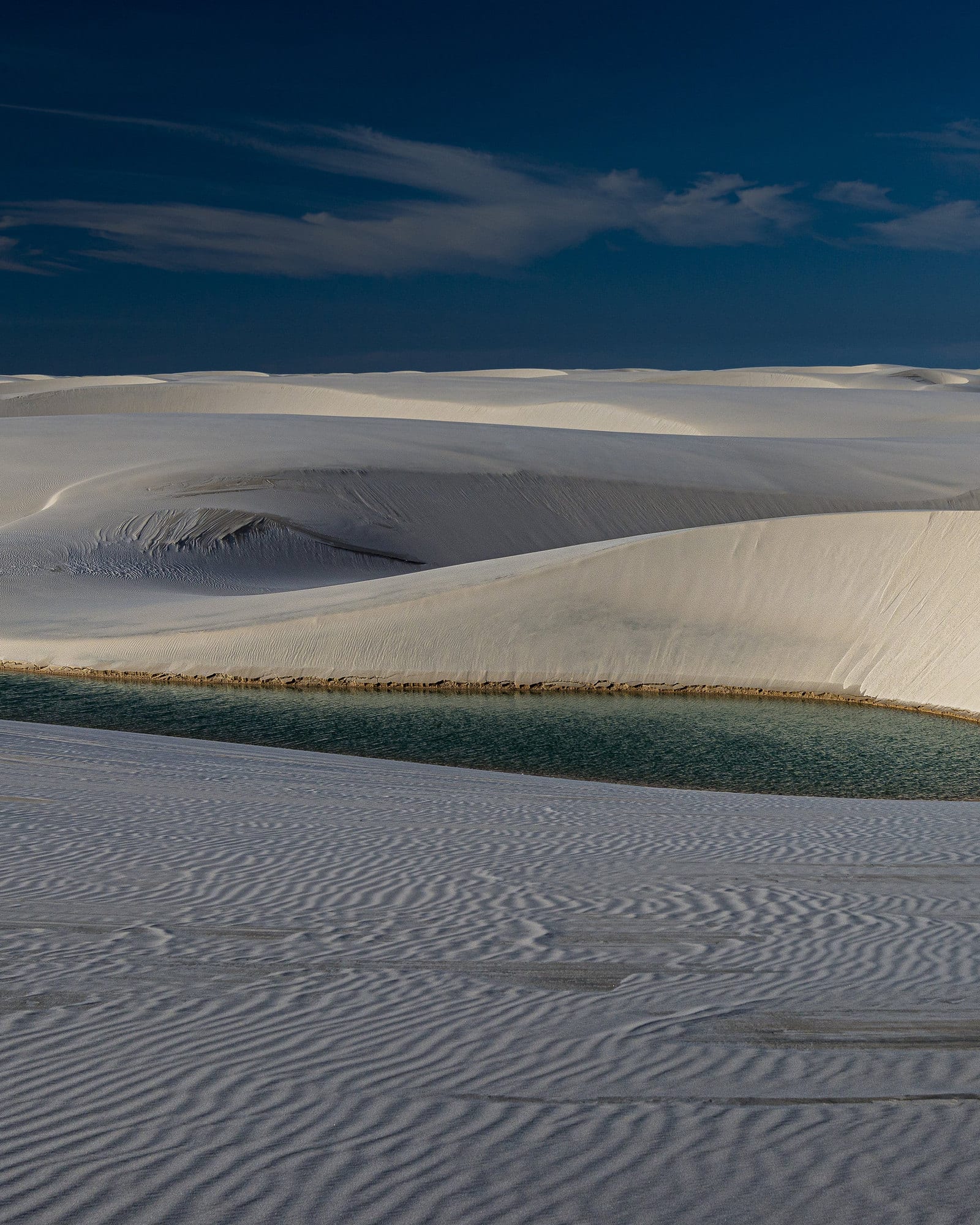 Lagoa de água azul entre dunas de areia branca nos Lençóis Maranhenses.
