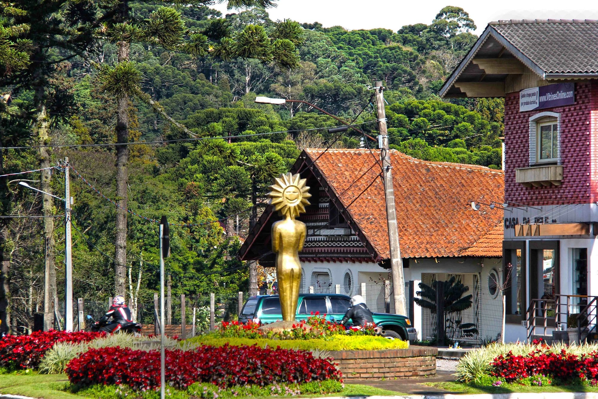 Casa de telhado vermelho com uma escultura dourada e canteiros de flores, no centro de Gramado.