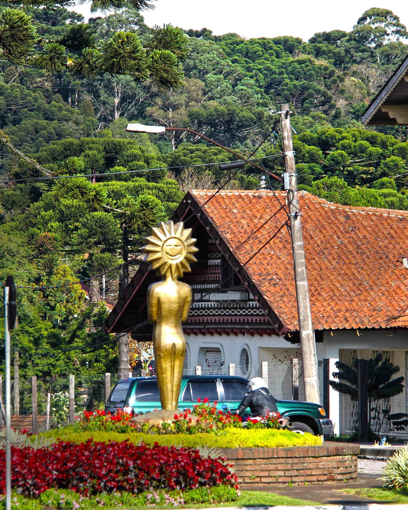 Casa de telhado vermelho com uma escultura dourada e canteiros de flores, no centro de Gramado.